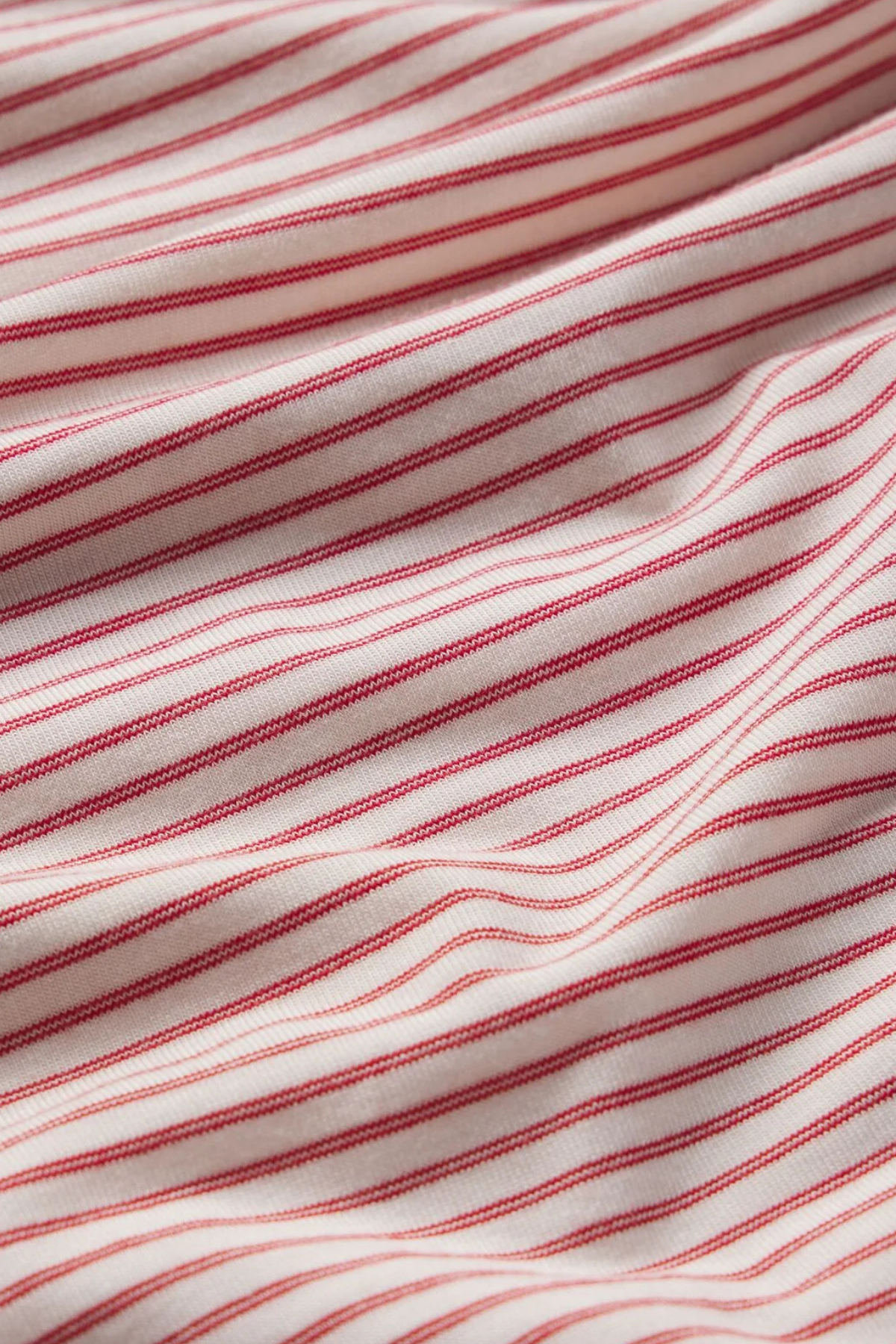 A close-up of a striped fabric with thin red stripes on a warm off-white or cream background.